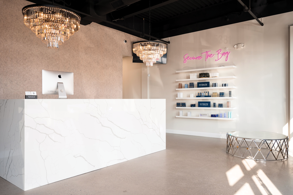 Face Candy's entance lobby. A marble check-out counter stands under two chandeliers and perpendicular to a wall displaying cosmetic items for sale.